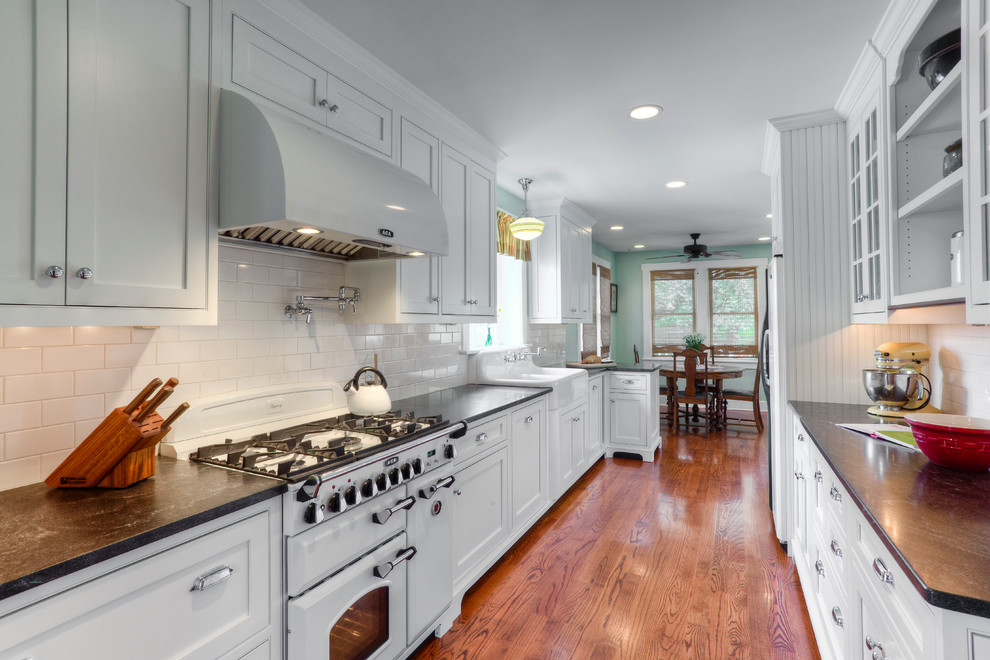 Traditional galley eat-in kitchen in Toronto with a farmhouse sink, shaker cabinets, white splashback, subway tile splashback and white appliances.