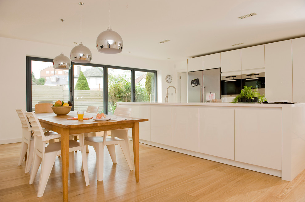 Photo of a mid-sized contemporary galley eat-in kitchen in Dorset with flat-panel cabinets, white cabinets, stainless steel appliances, light hardwood floors and with island.