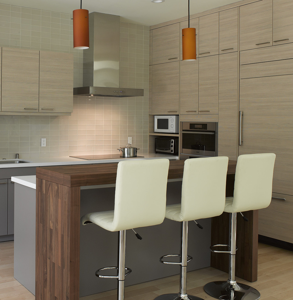 Inspiration for a small modern l-shaped eat-in kitchen in San Francisco with wood benchtops, flat-panel cabinets, panelled appliances, light wood cabinets, beige splashback, glass tile splashback, light hardwood floors, with island and beige floor.