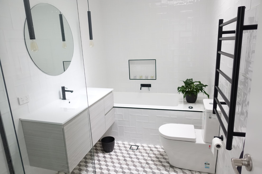 Photo of a mid-sized transitional bathroom in Sydney with grey cabinets, a drop-in tub, a corner shower, a one-piece toilet, white tile, ceramic tile, white walls, ceramic floors, an integrated sink and a hinged shower door.