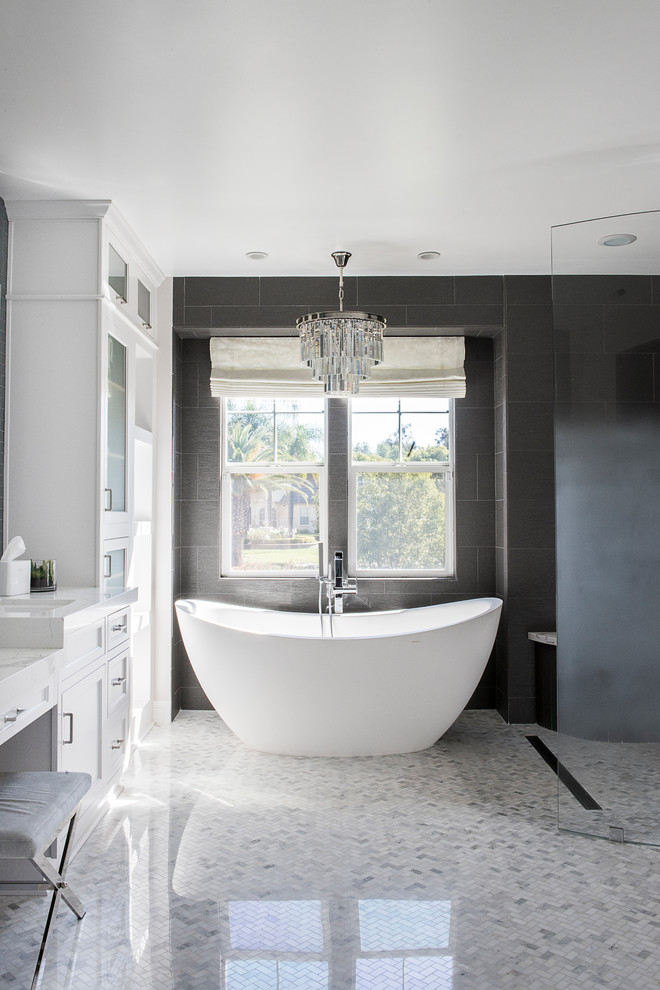 Photo of a mid-sized transitional master bathroom in Orange County with shaker cabinets, white cabinets, a freestanding tub, a curbless shower, gray tile, grey walls, an undermount sink, white floor, an open shower, white benchtops, porcelain tile, marble floors and engineered quartz benchtops.