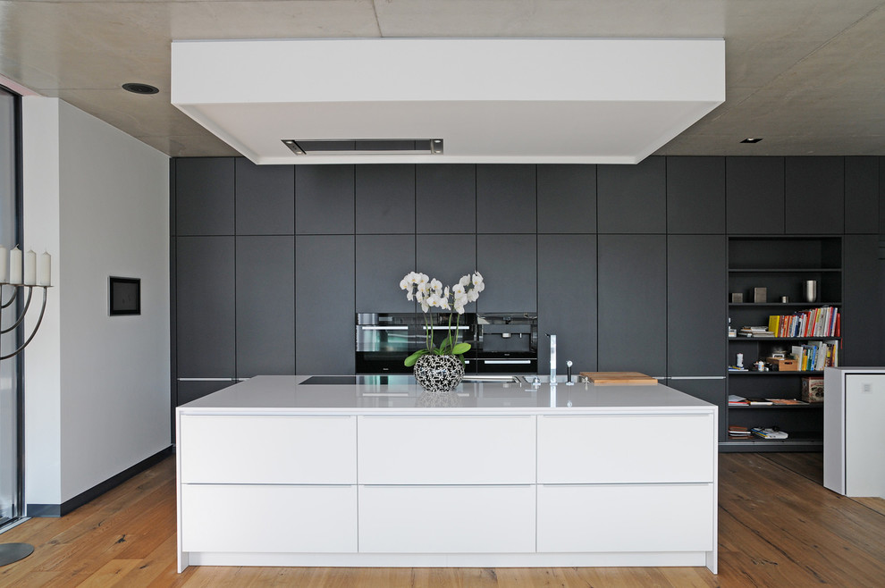 Design ideas for a mid-sized contemporary open plan kitchen in Dresden with flat-panel cabinets, medium hardwood floors, with island, a single-bowl sink and black appliances.