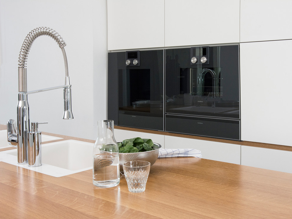 This is an example of a medium sized contemporary single-wall open plan kitchen in Berlin with a double-bowl sink, flat-panel cabinets, white cabinets, wood worktops, white splashback and an island.
