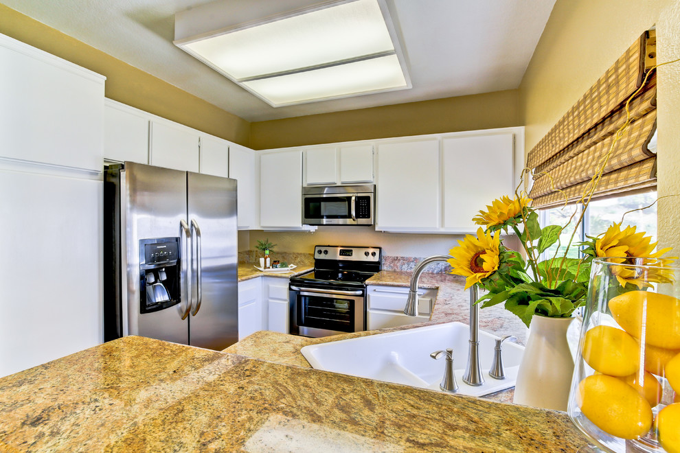 This is an example of a tropical eat-in kitchen in Orange County with a double-bowl sink, flat-panel cabinets, white cabinets, granite benchtops, stainless steel appliances, with island and dark hardwood floors.