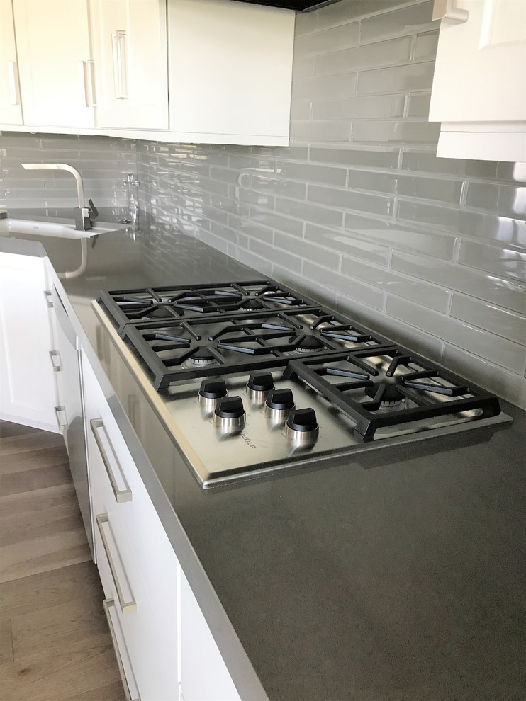 Inspiration for a mid-sized transitional l-shaped light wood floor and gray floor eat-in kitchen remodel with an undermount sink, recessed-panel cabinets, white cabinets, quartz countertops, gray backsplash, ceramic backsplash, stainless steel appliances and an island