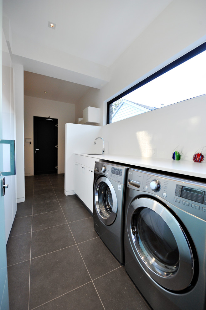 Large modern single-wall dedicated laundry room in Toronto with an undermount sink, flat-panel cabinets, white cabinets, solid surface benchtops, white walls, slate floors and a side-by-side washer and dryer.