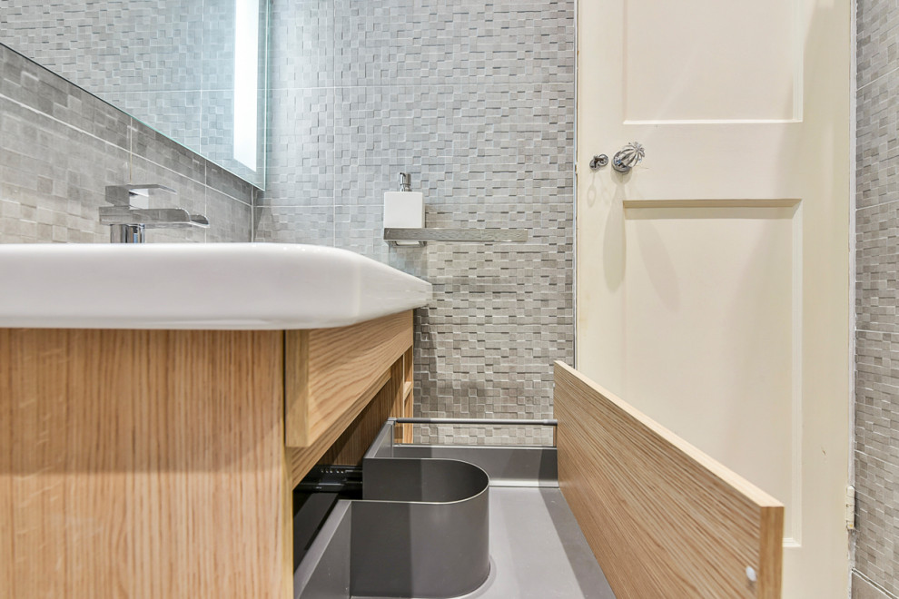 Design ideas for a small contemporary kids wet room bathroom in London with flat-panel cabinets, light wood cabinets, a wall-mount toilet, gray tile, ceramic tile, grey walls, porcelain floors, a wall-mount sink, grey floor and a hinged shower door.
