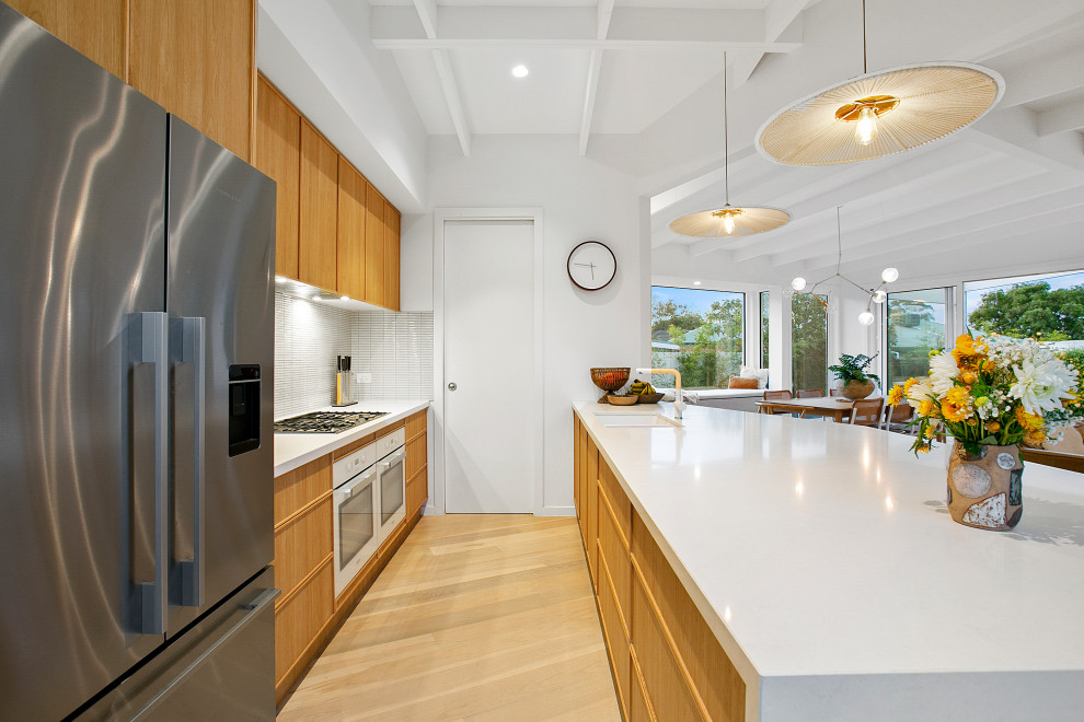Foto di una cucina stile marinaro con lavello sottopiano, ante in legno chiaro, top in quarzo composito, elettrodomestici bianchi, parquet chiaro e top bianco