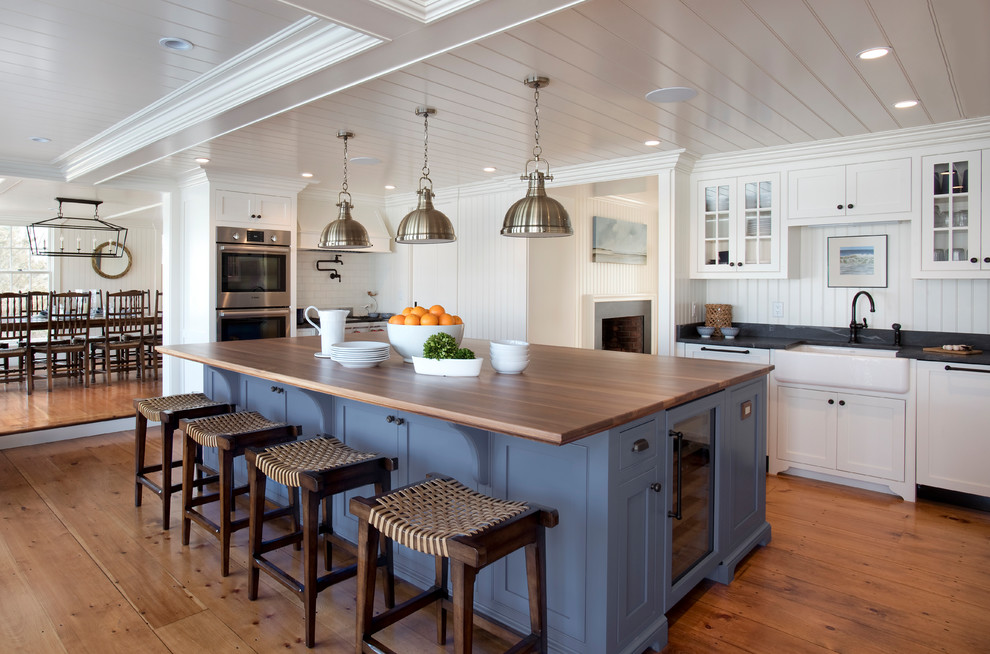 Inspiration for a beach style l-shaped eat-in kitchen in Boston with a farmhouse sink, shaker cabinets, blue cabinets, wood benchtops, white splashback, panelled appliances, medium hardwood floors, with island, brown floor and brown benchtop.