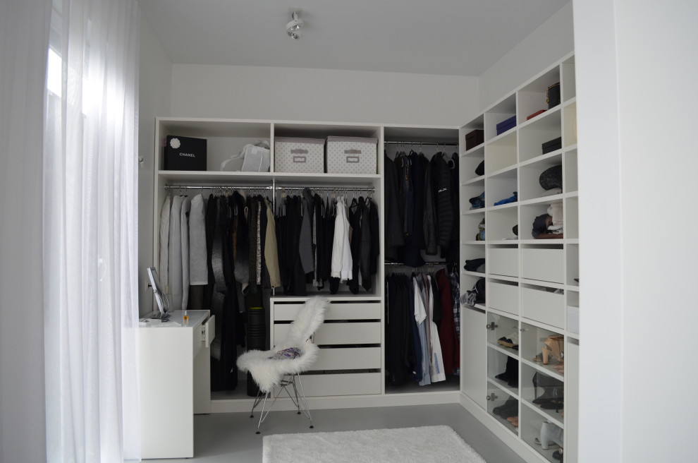 This is an example of a small modern gender-neutral walk-in wardrobe with white cabinets, concrete floors and grey floor.
