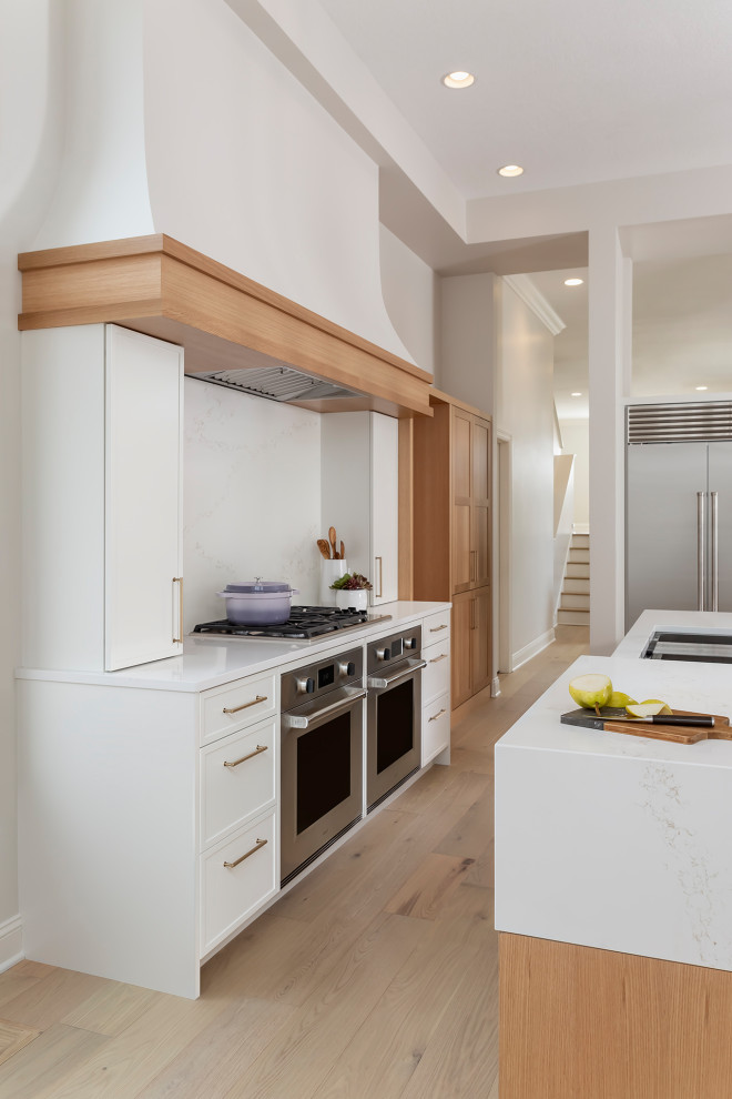 Inredning av ett klassiskt stort vit linjärt vitt kök med öppen planlösning, med en undermonterad diskho, släta luckor, vita skåp, bänkskiva i kvarts, vitt stänkskydd, rostfria vitvaror, ljust trägolv, flera köksöar och brunt golv
