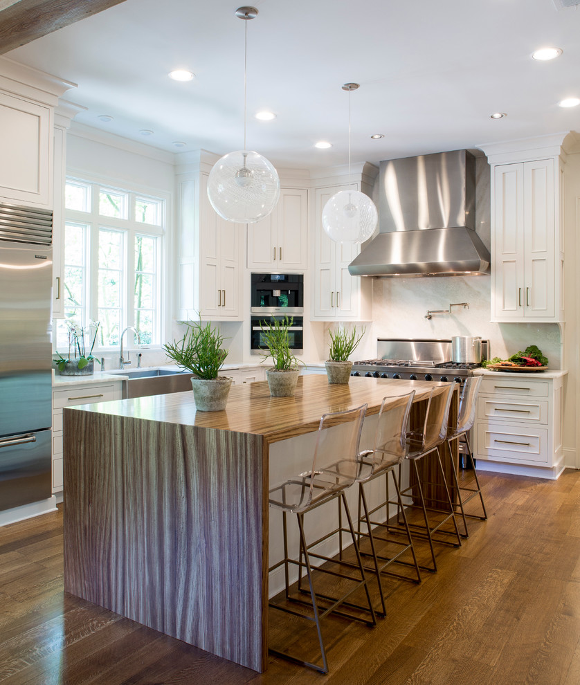 Large transitional l-shaped eat-in kitchen in Philadelphia with a farmhouse sink, beaded inset cabinets, white cabinets, white splashback, stainless steel appliances, medium hardwood floors, with island, stone slab splashback and brown floor.