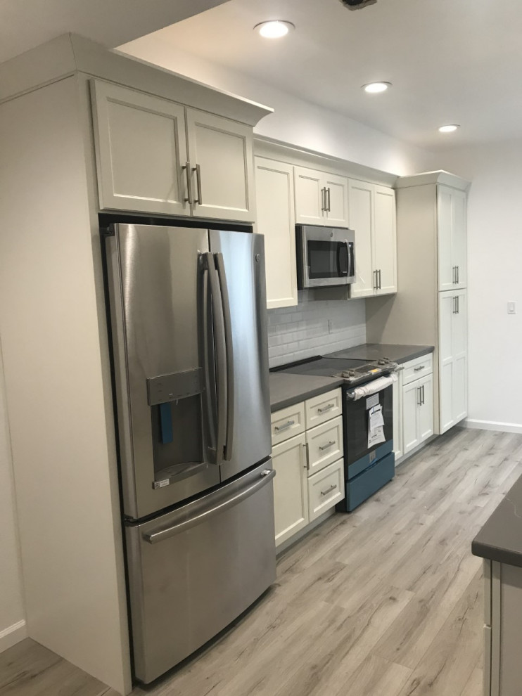 Small transitional galley kitchen pantry in Los Angeles with a farmhouse sink, shaker cabinets, white cabinets, quartzite benchtops, grey splashback, subway tile splashback, stainless steel appliances, vinyl floors, no island, grey floor and grey benchtop.