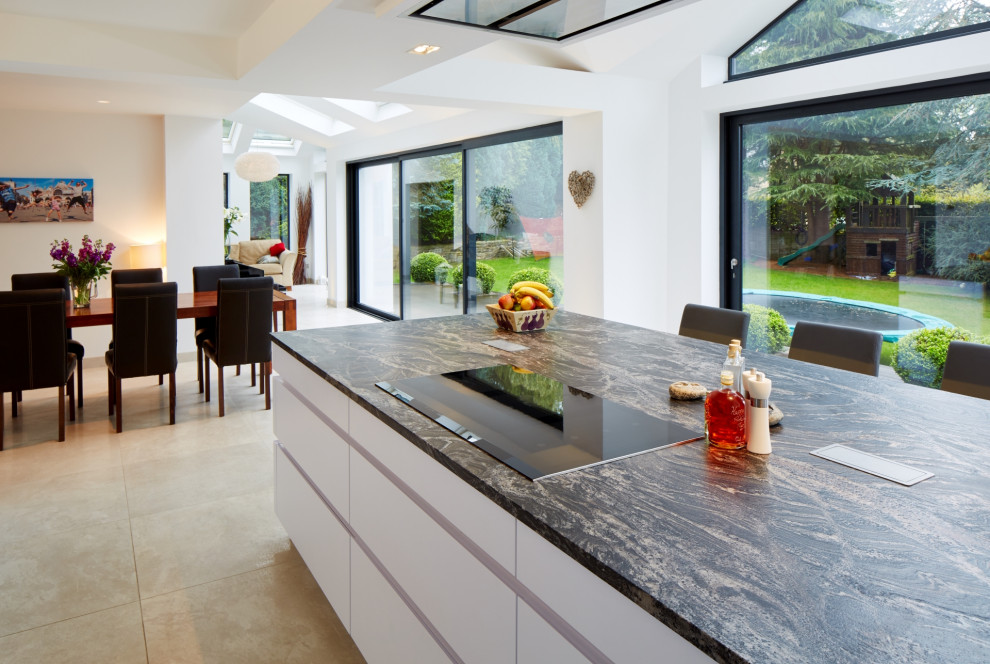 Mid-sized contemporary single-wall eat-in kitchen in Other with flat-panel cabinets, white cabinets, granite benchtops, metallic splashback, mirror splashback, panelled appliances, with island and blue benchtop.