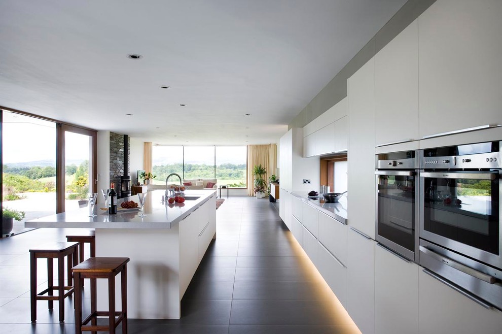 Inspiration for a large contemporary single-wall open plan kitchen in Other with a single-bowl sink, flat-panel cabinets, white cabinets, granite benchtops, white splashback, glass sheet splashback, stainless steel appliances, ceramic floors and with island.