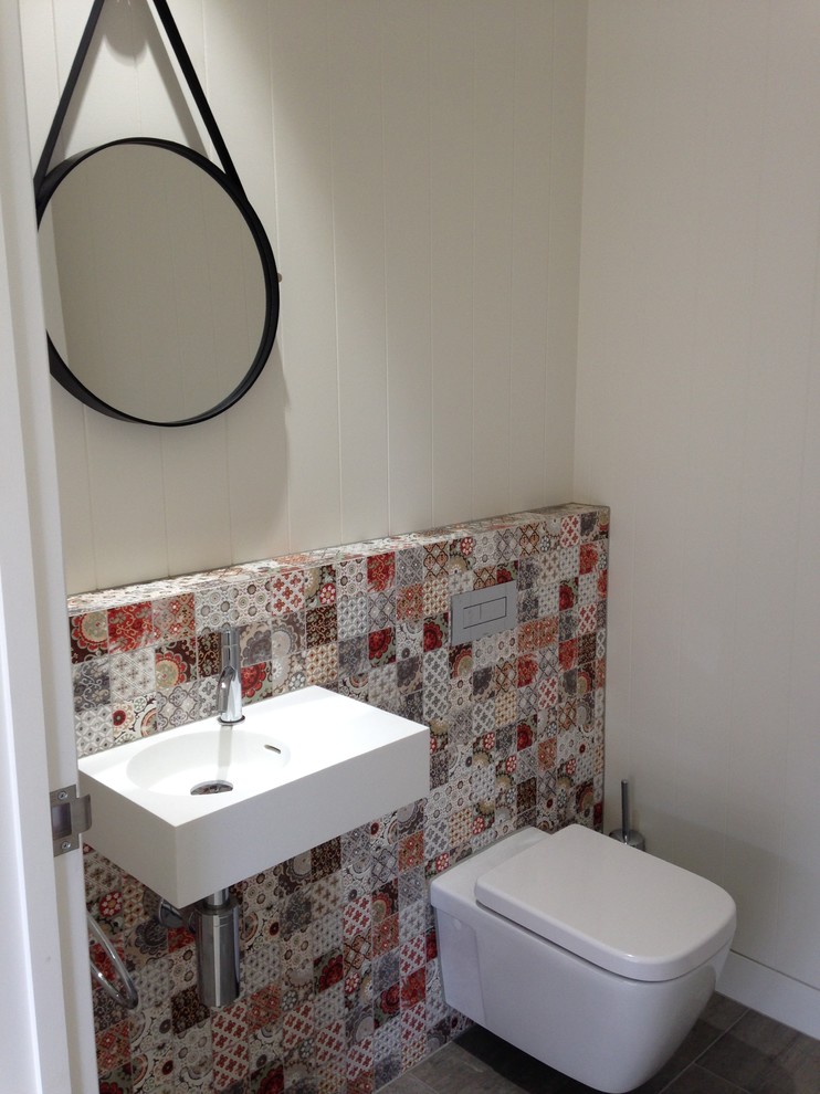 This is an example of a beach style powder room in Sunshine Coast with a wall-mount sink, a wall-mount toilet, multi-coloured tile, white walls, porcelain floors and ceramic tile.