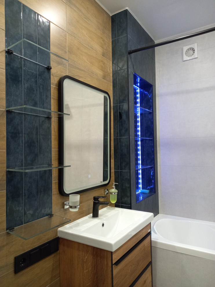 Пример оригинального дизайна: маленькая главная ванная комната в белых тонах с отделкой деревом: освещение в современном стиле с плоскими фасадами, фасадами цвета дерева среднего тона, ванной в нише, душем над ванной, инсталляцией, синей плиткой, плиткой под дерево, бежевыми стенами, полом из керамогранита, накладной раковиной, серым полом, шторкой для ванной, тумбой под одну раковину и подвесной тумбой для на участке и в саду
