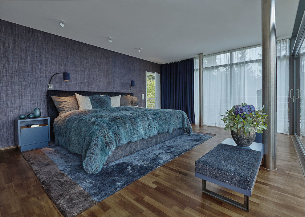 This is an example of a large contemporary master bedroom in Berlin with blue walls, medium hardwood floors, no fireplace and brown floor.