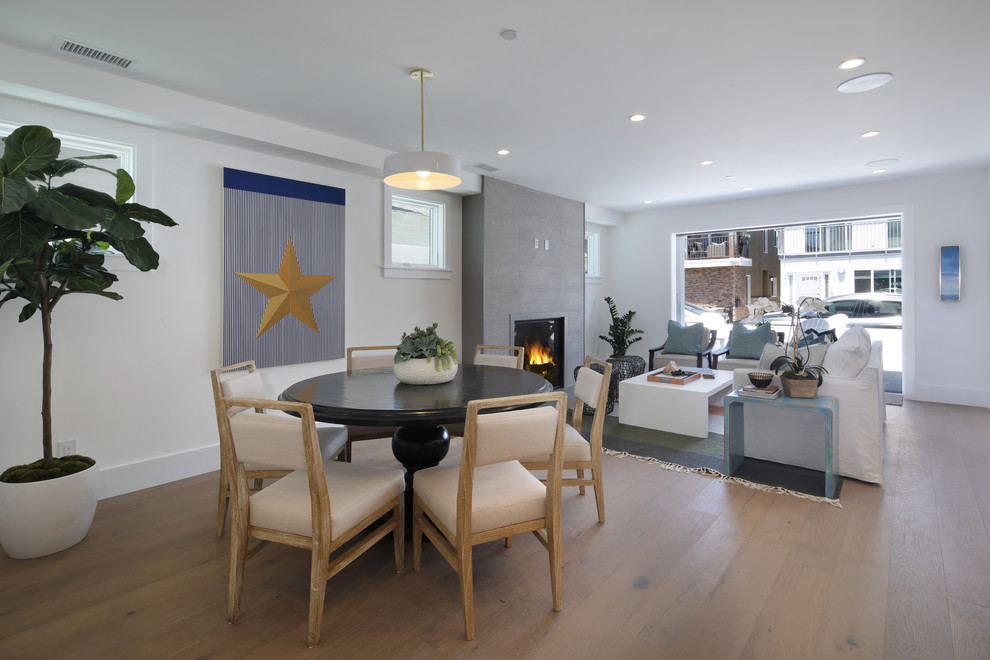 This is an example of a mid-sized beach style open plan dining in Orange County with white walls, medium hardwood floors, a standard fireplace, a concrete fireplace surround and brown floor.