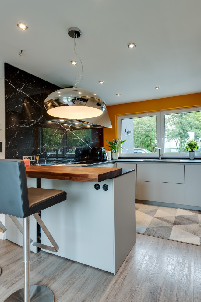 This is an example of a large traditional u-shaped open plan kitchen in Hamburg with an integrated sink, flat-panel cabinets, white cabinets, solid surface benchtops, black splashback, marble splashback, black appliances, terrazzo floors, a peninsula, multi-coloured floor, black benchtop and recessed.