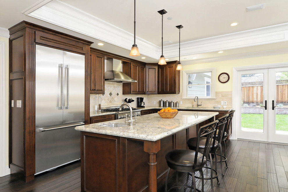 This is an example of a traditional l-shaped kitchen in San Francisco with stainless steel appliances, raised-panel cabinets, dark wood cabinets and granite benchtops.