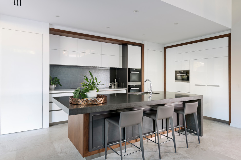 Large contemporary galley open plan kitchen in Perth with an undermount sink, recessed-panel cabinets, white cabinets, quartz benchtops, metallic splashback, ceramic splashback, stainless steel appliances, with island, grey floor, black benchtop and limestone floors.