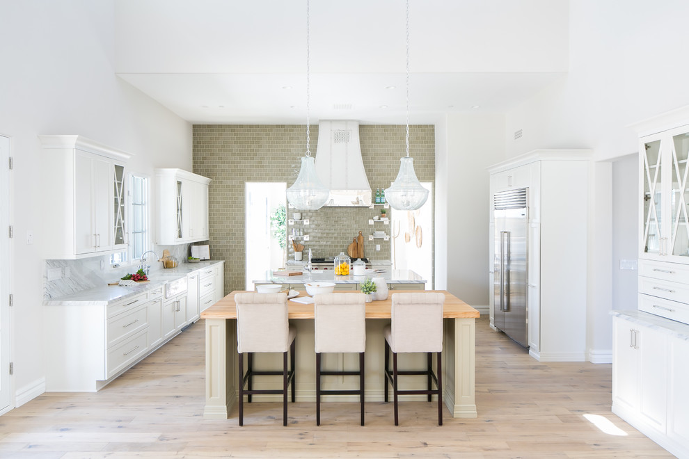 Eat-in kitchen - large transitional light wood floor and brown floor eat-in kitchen idea in Phoenix with a farmhouse sink, white cabinets, marble countertops, green backsplash, ceramic backsplash, stainless steel appliances and two islands