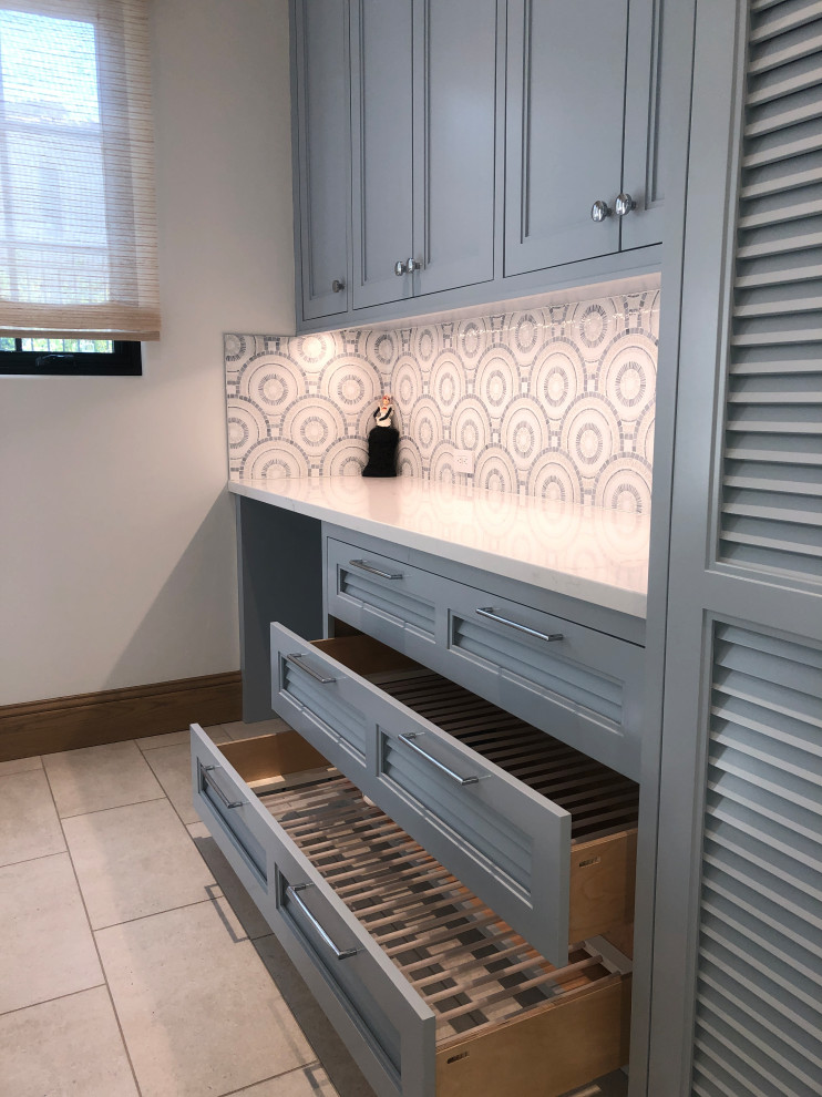 Inspiration for a large transitional u-shaped porcelain tile and gray floor dedicated laundry room remodel in San Diego with a farmhouse sink, shaker cabinets, blue cabinets, quartz countertops, blue backsplash, mosaic tile backsplash, white walls, a side-by-side washer/dryer and white countertops