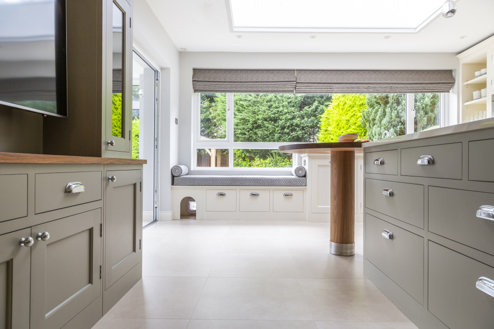 This is an example of a large traditional u-shaped separate kitchen in Hertfordshire with an undermount sink, shaker cabinets, white splashback, engineered quartz splashback, stainless steel appliances, ceramic floors, with island and white benchtop.