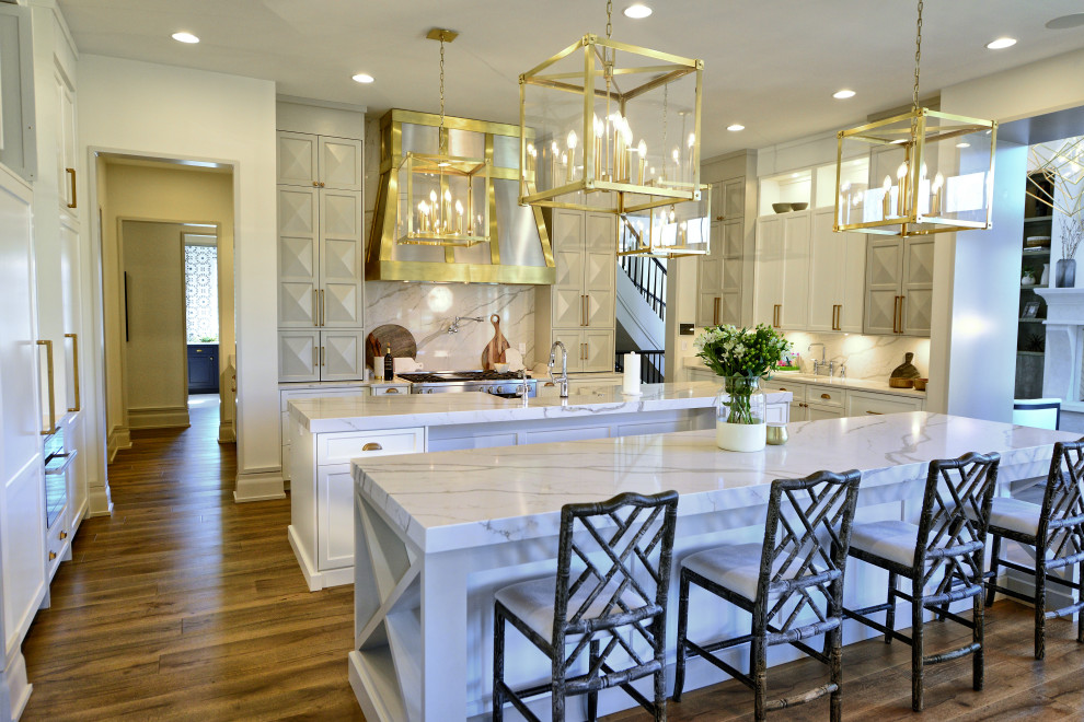 Large transitional eat-in kitchen in Indianapolis with a farmhouse sink, recessed-panel cabinets, white cabinets, marble benchtops, white splashback, marble splashback, stainless steel appliances, medium hardwood floors, multiple islands, multi-coloured floor and white benchtop.
