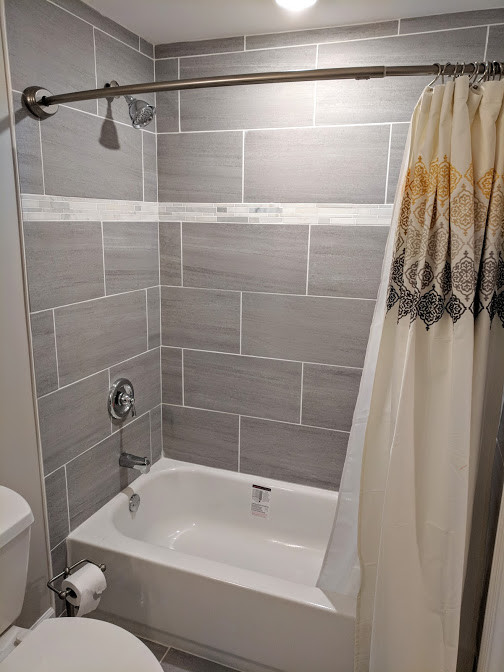 Inspiration for a mid-sized transitional kids bathroom in Chicago with recessed-panel cabinets, grey cabinets, an alcove tub, a shower/bathtub combo, a two-piece toilet, gray tile, porcelain tile, grey walls, porcelain floors, an undermount sink, marble benchtops, grey floor, a shower curtain and white benchtops.