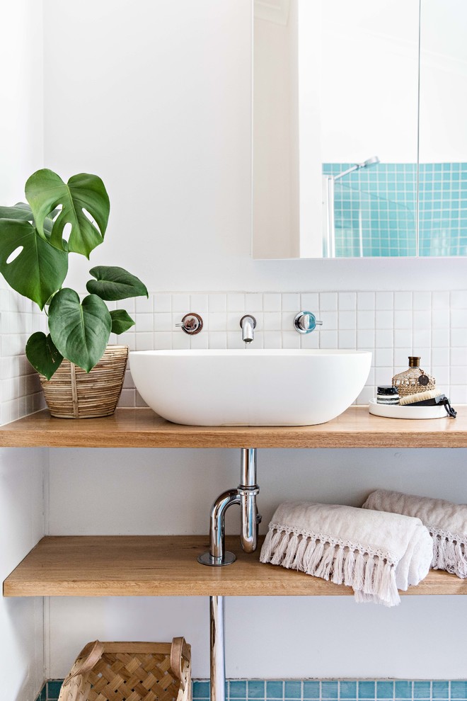This is an example of a beach style bathroom in Wollongong with open cabinets, medium wood cabinets, blue tile, mosaic tile, white walls, a vessel sink, wood benchtops and brown benchtops.