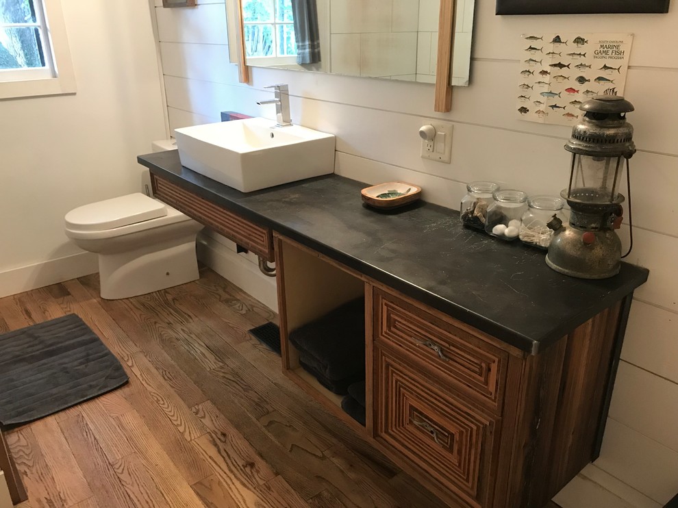 Inspiration for a mid-sized country 3/4 bathroom in Charleston with furniture-like cabinets, distressed cabinets, an open shower, a one-piece toilet, white walls, medium hardwood floors, a vessel sink, stainless steel benchtops, brown floor and black benchtops.