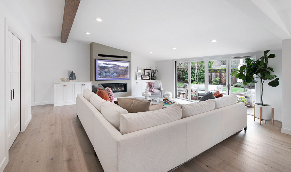 Design ideas for a large modern open concept family room in San Francisco with white walls, light hardwood floors, a ribbon fireplace, a metal fireplace surround, a wall-mounted tv, beige floor and exposed beam.