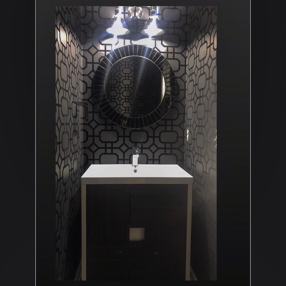 This is an example of a mid-sized powder room in Other with furniture-like cabinets, black cabinets, black walls, medium hardwood floors, an integrated sink, glass benchtops, brown floor, white benchtops, a two-piece toilet, wallpaper and a freestanding vanity.