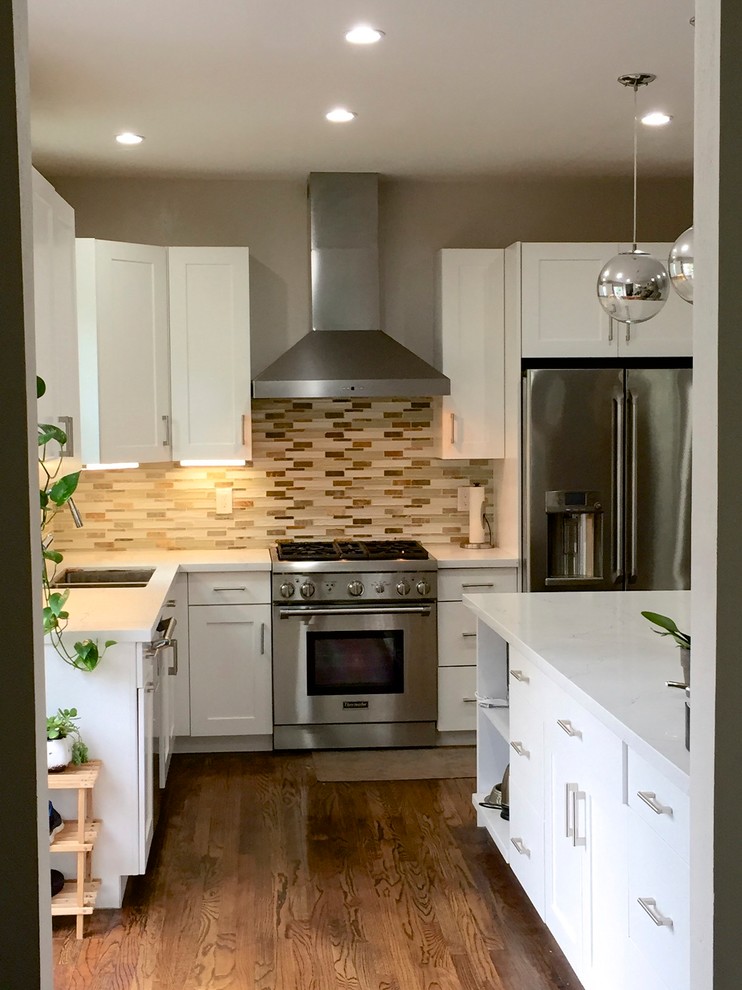 This is an example of a mid-sized transitional l-shaped open plan kitchen in San Francisco with an undermount sink, recessed-panel cabinets, white cabinets, quartzite benchtops, multi-coloured splashback, glass tile splashback, stainless steel appliances, medium hardwood floors, a peninsula and brown floor.