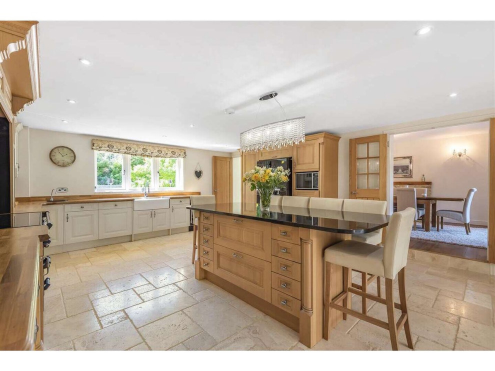 Design ideas for a large country u-shaped kitchen in Gloucestershire with a drop-in sink, raised-panel cabinets, medium wood cabinets, marble benchtops, black appliances, ceramic floors, with island, beige floor, black benchtop and recessed.