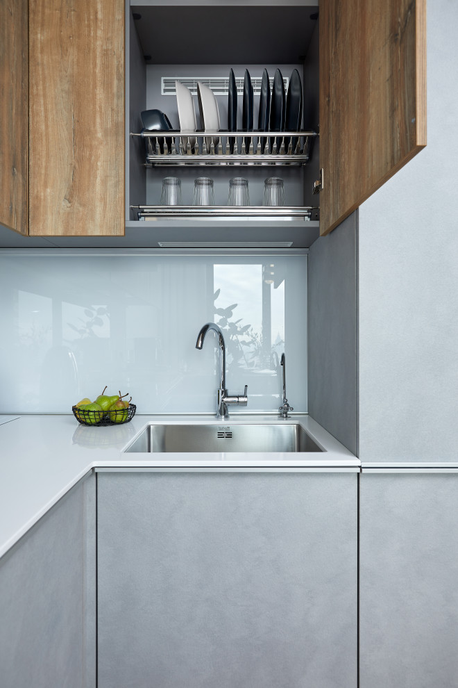 Photo of a small u-shaped open plan kitchen in Moscow with a single-bowl sink, grey cabinets, solid surface benchtops, white splashback, glass sheet splashback, panelled appliances, no island and white benchtop.