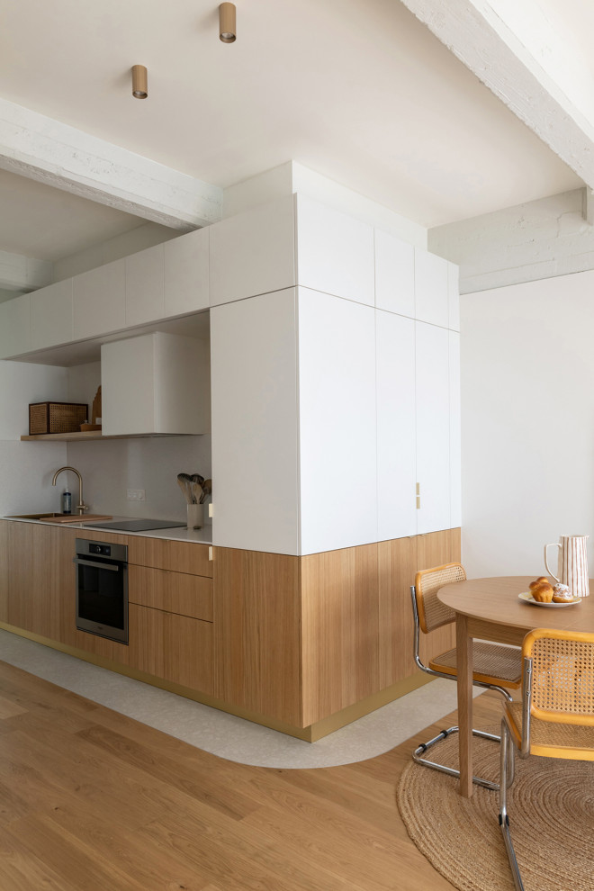 Mid-sized contemporary single-wall open plan kitchen in Strasbourg with a single-bowl sink, beaded inset cabinets, light wood cabinets, solid surface benchtops, white splashback, terrazzo floors and white benchtop.