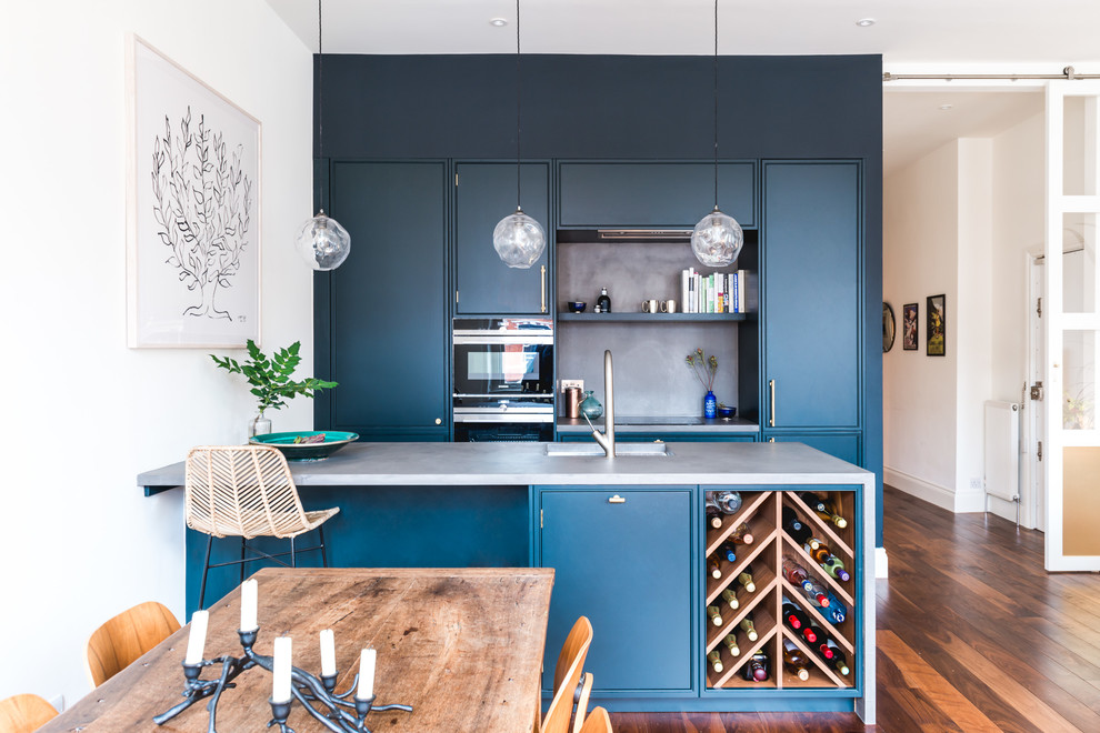 Inspiration for a small contemporary single-wall open plan kitchen in London with an undermount sink, flat-panel cabinets, blue cabinets, concrete benchtops, black appliances, dark hardwood floors, brown floor, grey splashback and a peninsula.