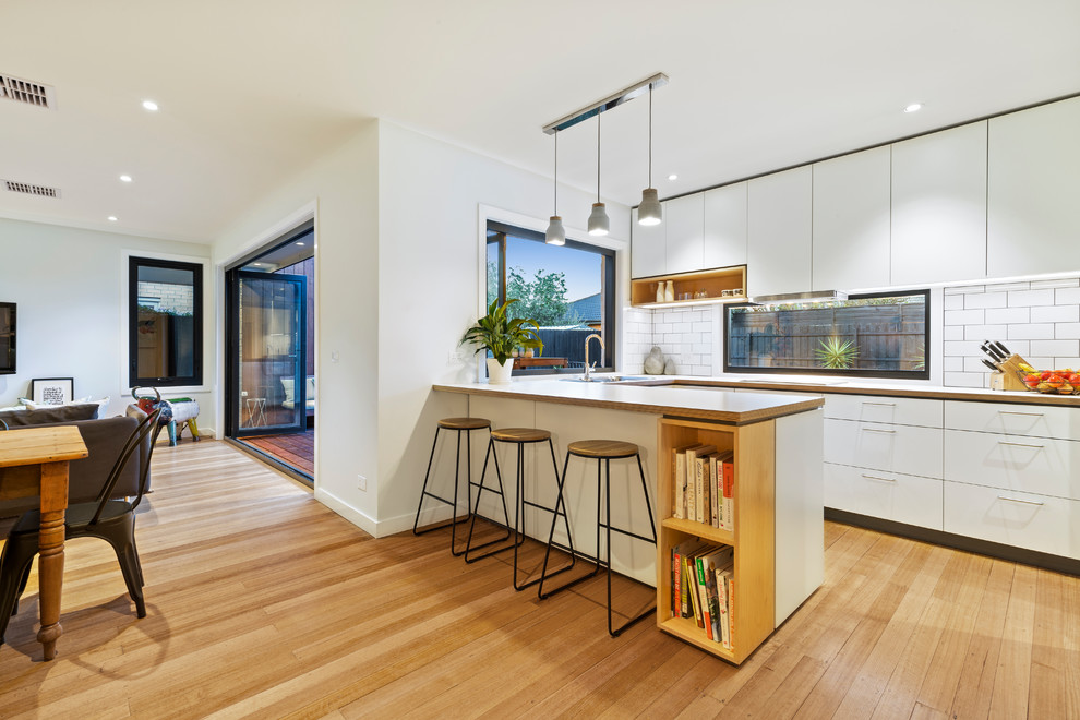 Design ideas for a small contemporary u-shaped open plan kitchen in Melbourne with a drop-in sink, raised-panel cabinets, white cabinets, marble benchtops, white splashback, ceramic splashback, stainless steel appliances, light hardwood floors, with island, yellow floor and white benchtop.