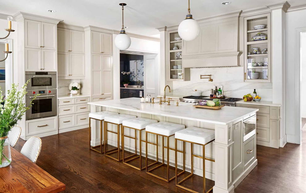 Photo of an expansive traditional l-shaped eat-in kitchen in Austin with an undermount sink, recessed-panel cabinets, grey cabinets, marble benchtops, white splashback, marble splashback, stainless steel appliances, medium hardwood floors, with island, brown floor and white benchtop.