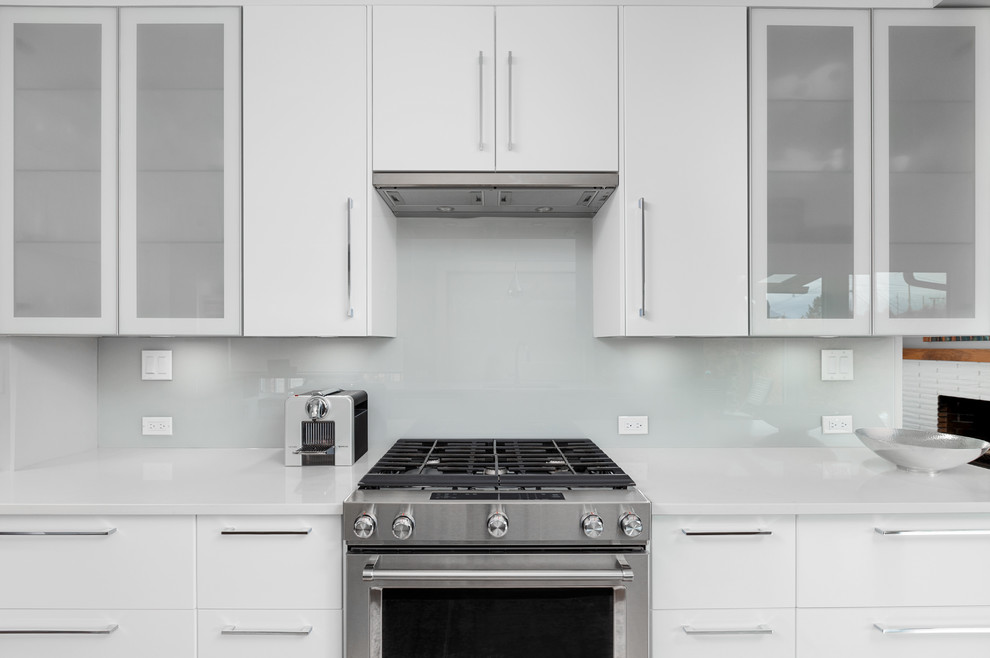 This is an example of a mid-sized contemporary galley eat-in kitchen in Vancouver with a double-bowl sink, flat-panel cabinets, white cabinets, quartz benchtops, grey splashback, glass sheet splashback, stainless steel appliances, light hardwood floors, a peninsula, grey floor and white benchtop.