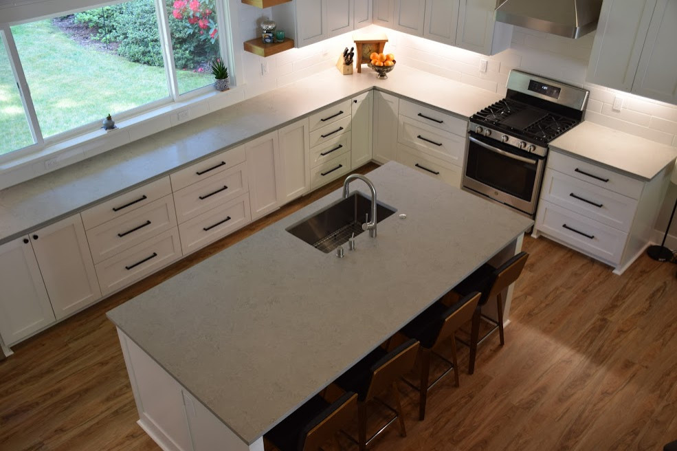 Large contemporary l-shaped open plan kitchen in Seattle with an undermount sink, shaker cabinets, white cabinets, quartz benchtops, white splashback, subway tile splashback, stainless steel appliances, laminate floors, with island, multi-coloured floor, grey benchtop and vaulted.