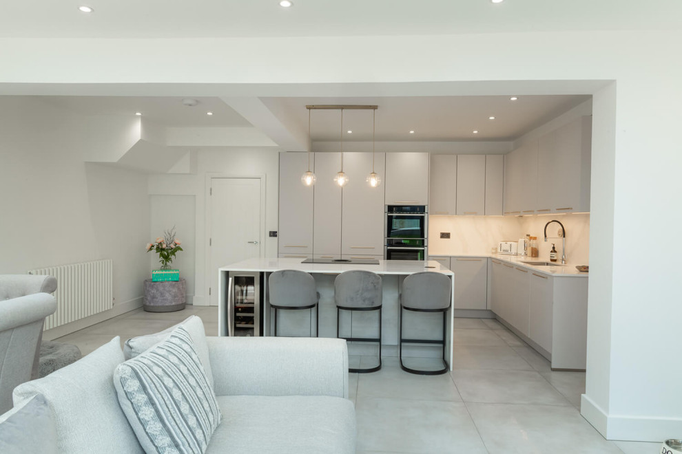 Design ideas for a mid-sized modern l-shaped eat-in kitchen in London with an integrated sink, flat-panel cabinets, white cabinets, marble benchtops, black appliances, with island, white benchtop and recessed.