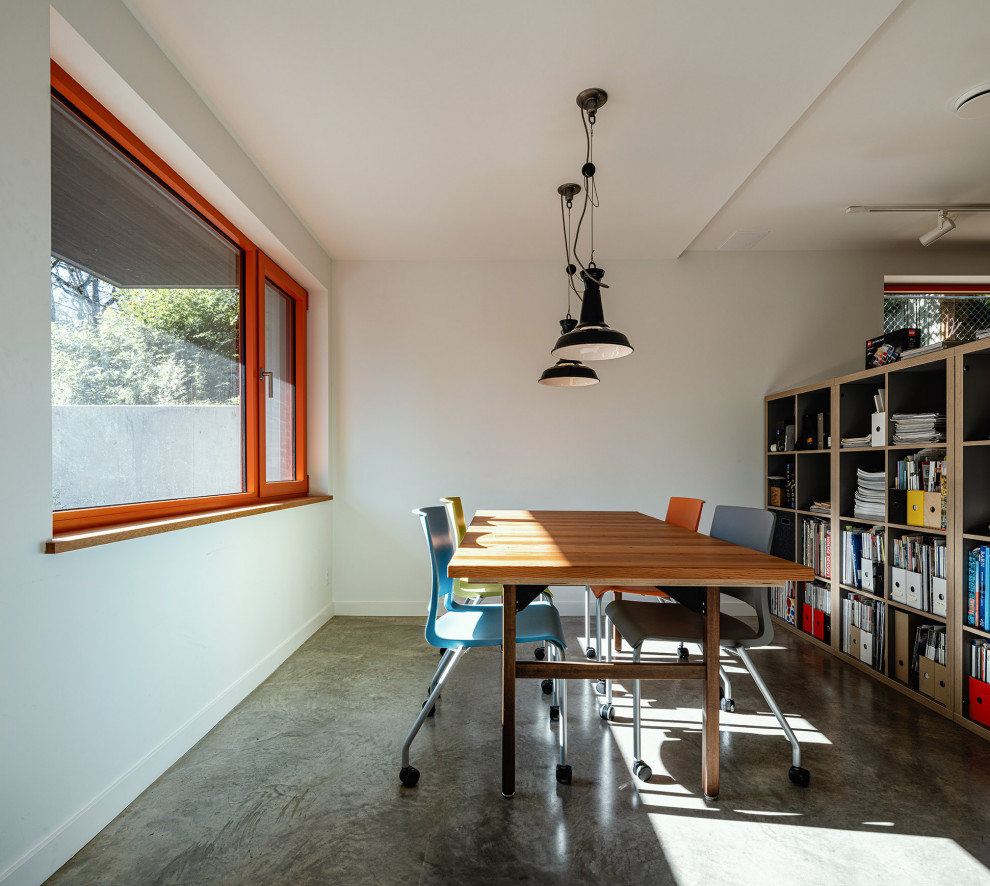 Imagen de estudio actual de tamaño medio con paredes blancas, suelo de cemento, escritorio independiente y suelo gris