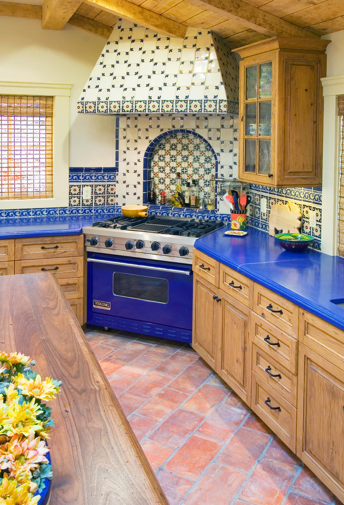 This is an example of a mid-sized eclectic l-shaped eat-in kitchen in San Francisco with raised-panel cabinets, with island, light wood cabinets, terra-cotta floors, an undermount sink, solid surface benchtops, multi-coloured splashback, ceramic splashback, coloured appliances and red floor.