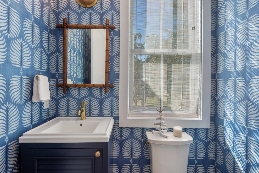 Photo of a coastal cloakroom in New Orleans with shaker cabinets, blue cabinets, a two-piece toilet, blue walls, light hardwood flooring, a built-in sink, beige floors, white worktops, a built in vanity unit and wallpapered walls.
