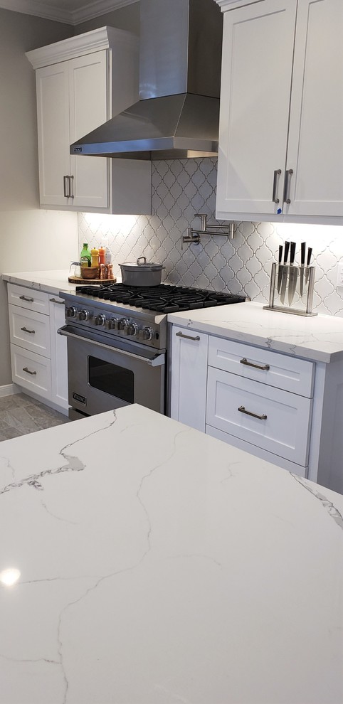 Photo of a mid-sized transitional galley separate kitchen in Houston with an undermount sink, shaker cabinets, white cabinets, quartz benchtops, white splashback, porcelain splashback, stainless steel appliances, ceramic floors, a peninsula, grey floor and white benchtop.