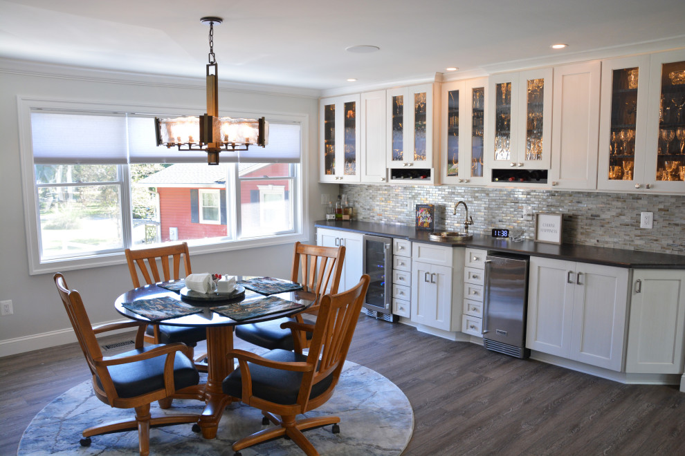 Bild på ett stort vintage vit linjärt vitt kök och matrum, med en rustik diskho, luckor med infälld panel, vita skåp, bänkskiva i kvarts, grått stänkskydd, rostfria vitvaror, en köksö och brunt golv